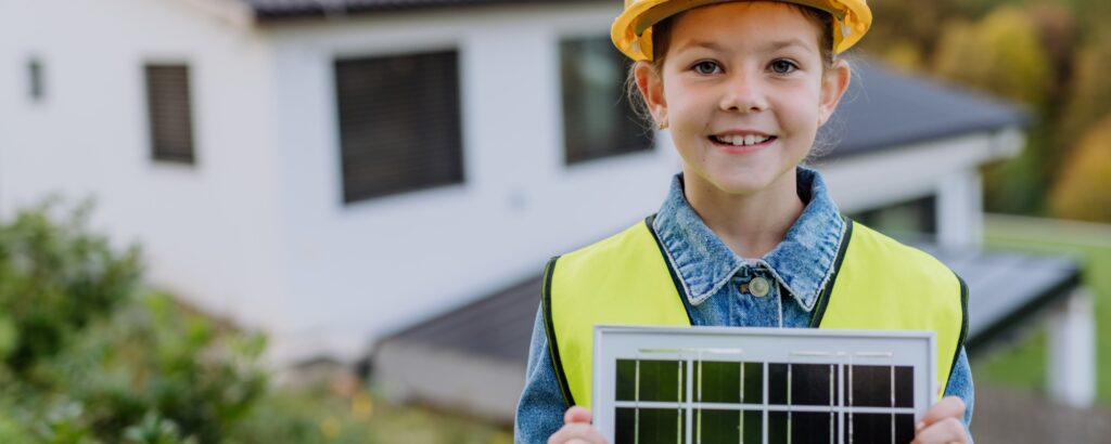 Dekoratives Bild: Kind mit einem Bauhelm auf dem Kopf hält kleines Solarpanel in der Hand.